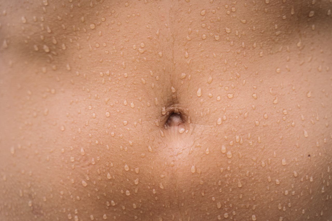A detailed close-up image of a human belly with water droplets on the skin, showcasing texture.