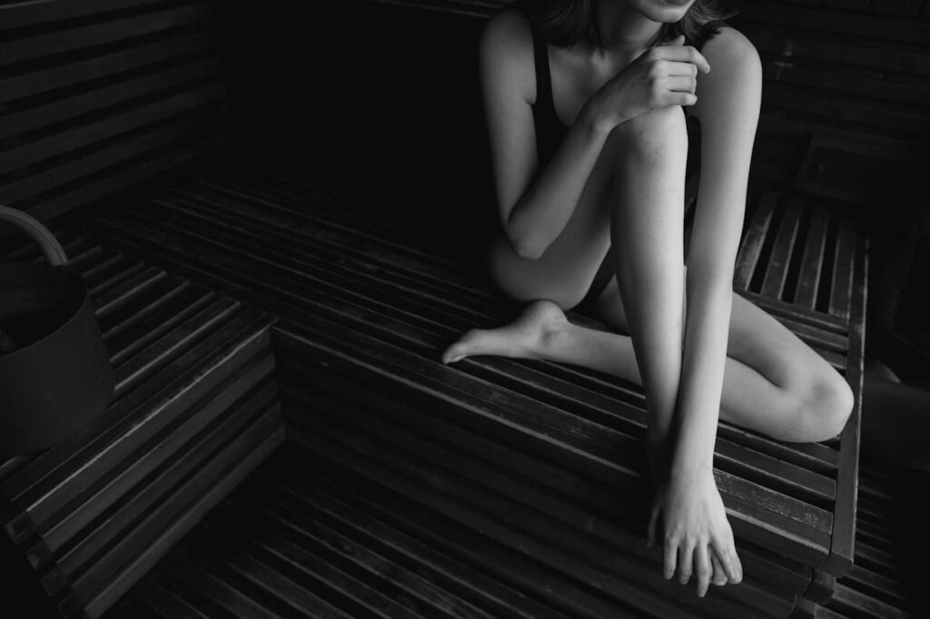 A woman in a bathing suit sits elegantly on wooden sauna benches the dark olive
