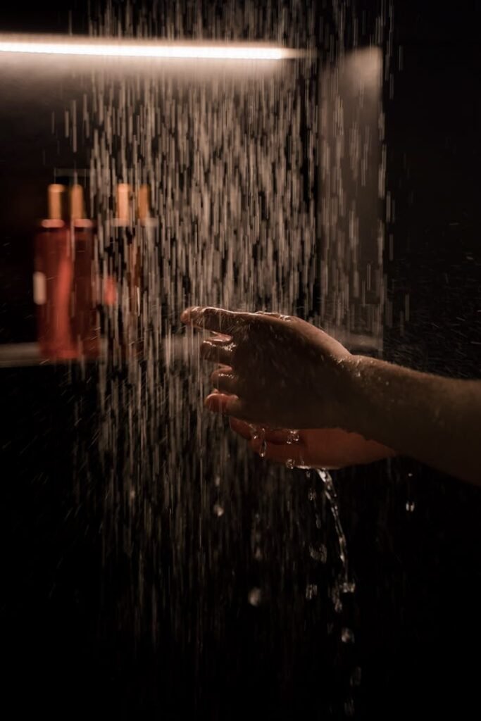 A tranquil hand under running water in a dimly lit shower setting, capturing moisture and ambiance.