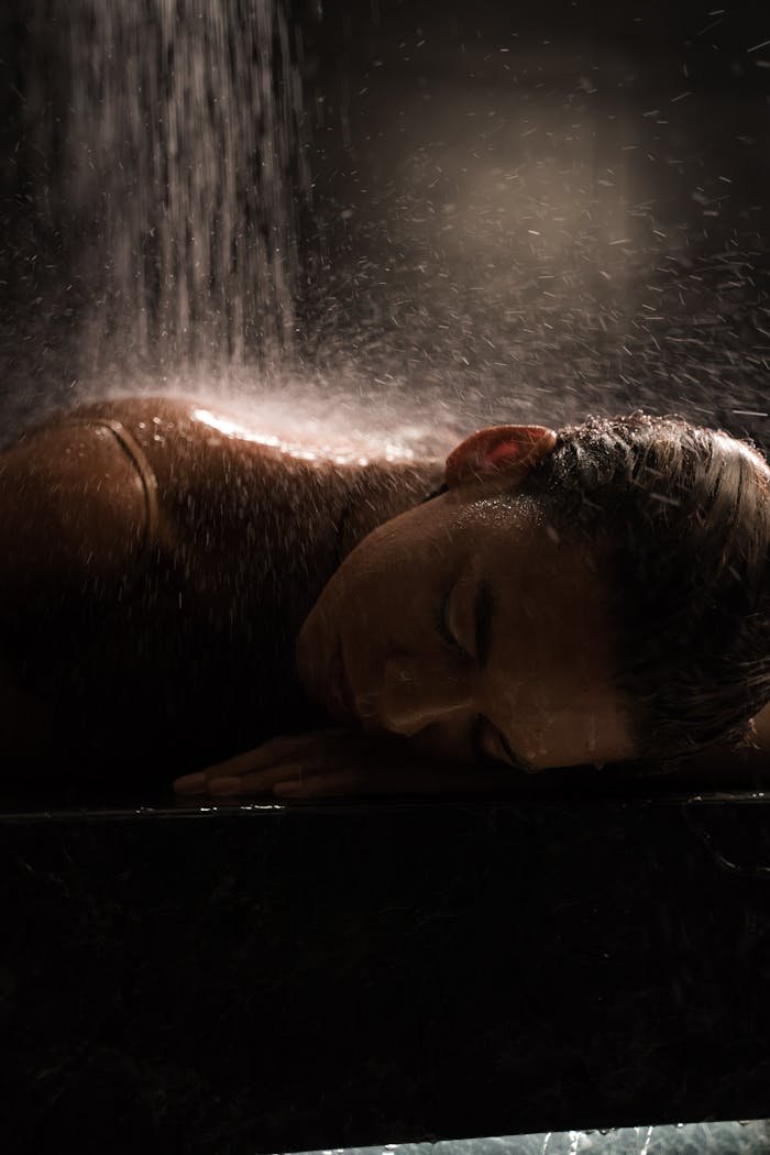 Woman enjoying a soothing shower, highlighting relaxation in a dimly lit setting.